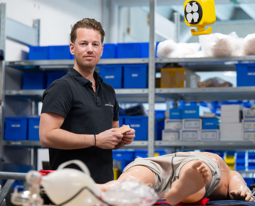 Mefina Mitarbeiter steht neben einer medizinischen Simulationspuppe bei Mefina Medical Mefina Mitarbeiter steht, in die Kamera schauend, neben einer medizinischen Simulationspuppe