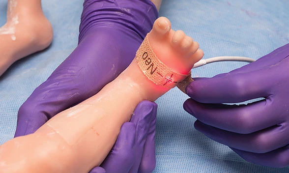 Gaumard-Super-Tory-S2220-spo2 Arzt hält Fuß eines Neugeborenen-Simulators und bringt Pflaster an