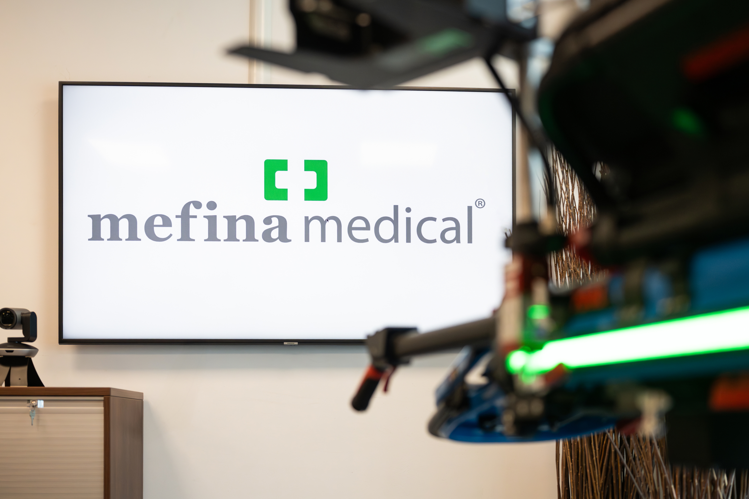 Mefina - Logo on the Tv Screen with medical stretcher in the foreground