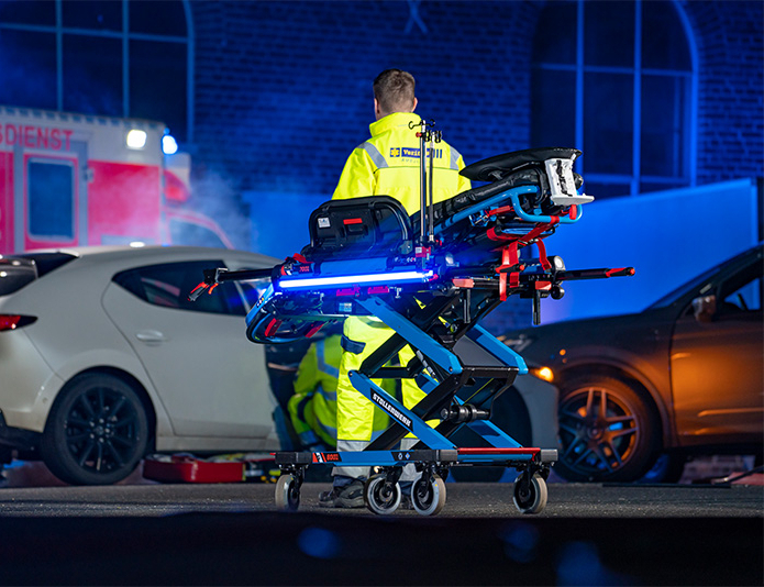 Stollenwerk CPS-Szenenbild bei Nacht Szenenbild mit Rettungssanitäter, welcher sich den Autounfall im Hintergrund anschaut + Rettungstrage CPS im Vordergrund.