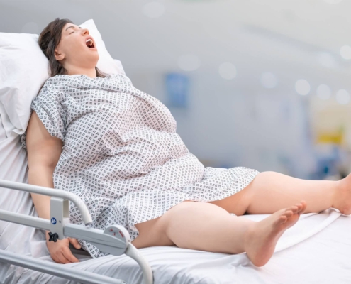 Große Aufnahme des bariatrischer Patientensimulator - R42 mit offenem Mund und gespreizten Beinen aufrecht in Krankenbett